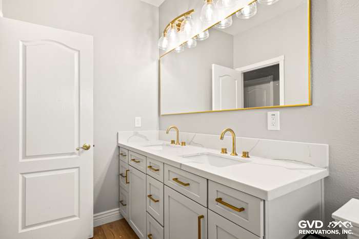 Modern guest bathroom with dual sinks, gold fixtures, gray cabinetry, and large mirror in El Dorado Hills remodel