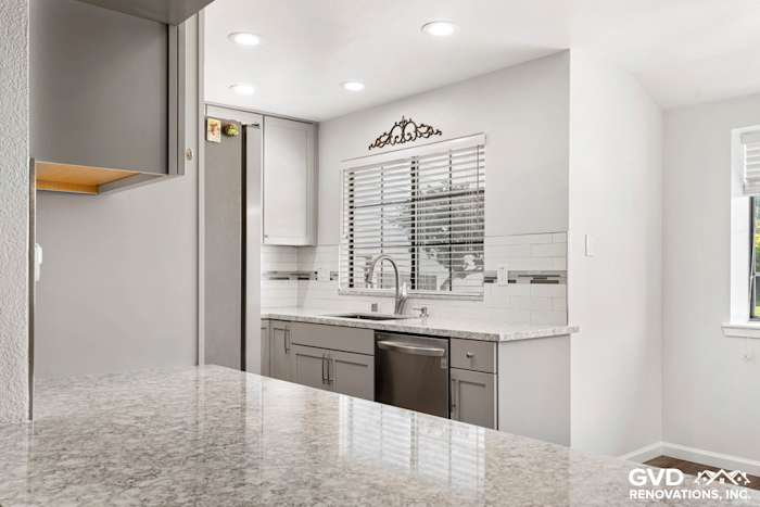 Modern kitchen with gray cabinetry, quartz countertops, and a stainless steel sink, featuring under-cabinet lighting