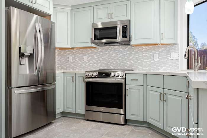 Modern kitchen in Cameron Park with light green cabinets, stainless steel appliances, and backsplash tiles