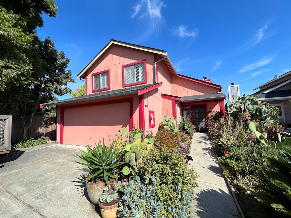 Two-story home in Sacramento with pink exterior, manicured landscaping, and bright blue sky
