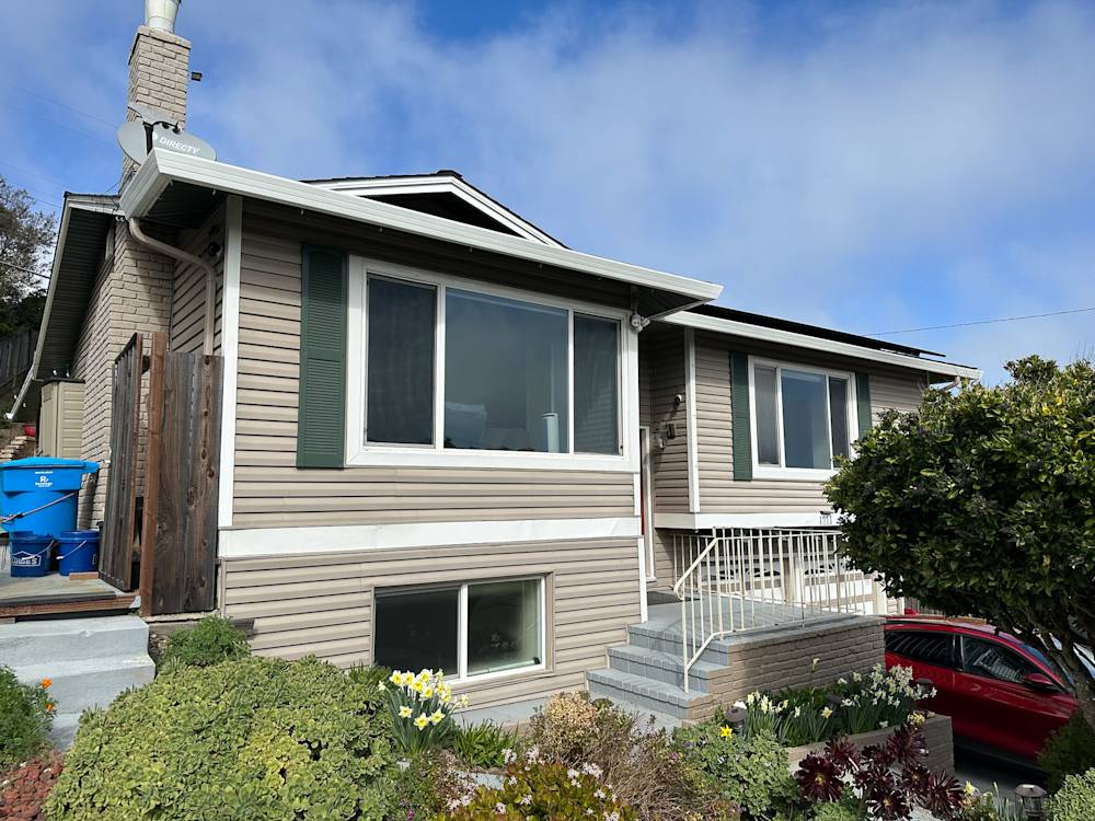 Bland exterior of a Sacramento home with beige siding and gray steps, surrounded by greenery and flowers