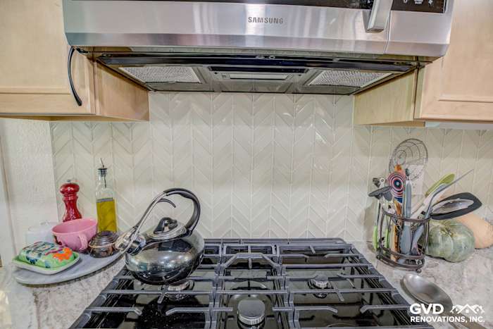 Modern kitchen featuring a Samsung range hood, herringbone backsplash, and gas cooktop with cookware and utensils