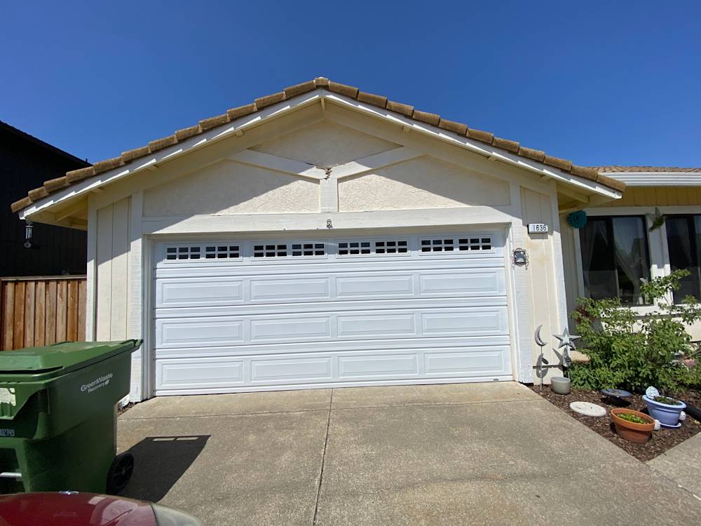Worn exterior of Sacramento home featuring a white garage door and light-colored walls