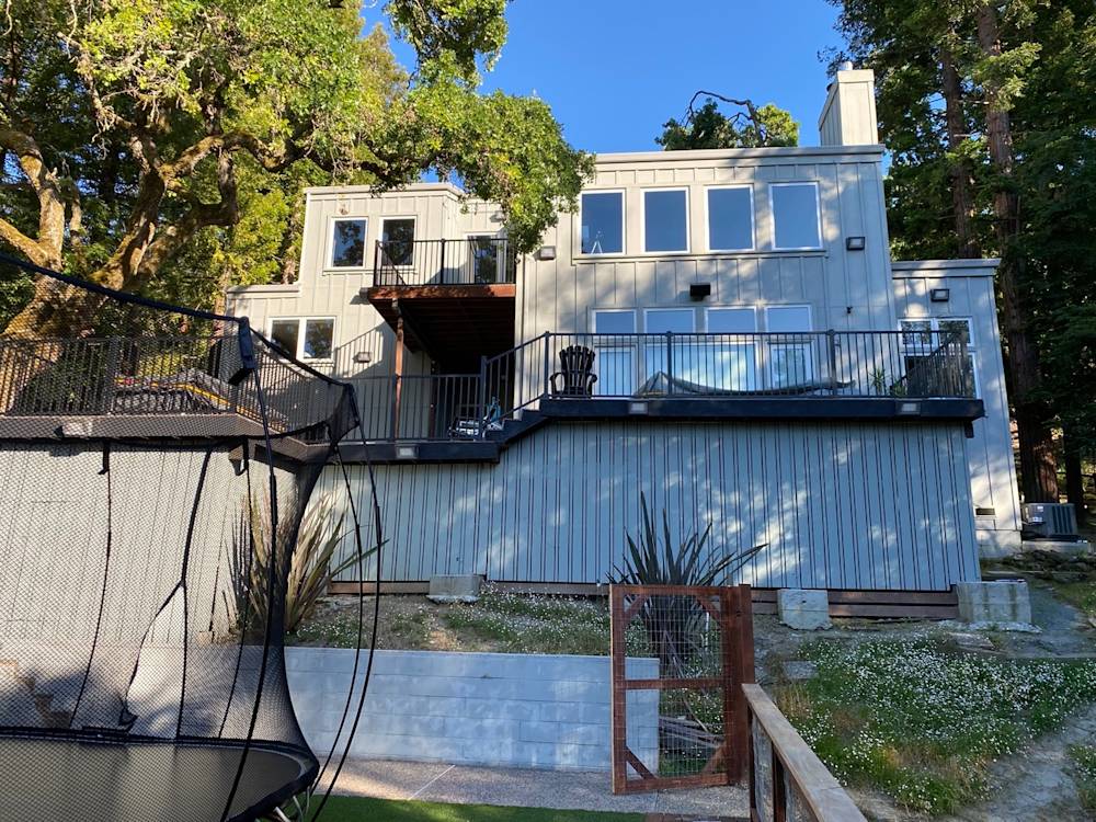 Two-story home with gray siding, large windows, and a wooden deck in Sacramento's greenery