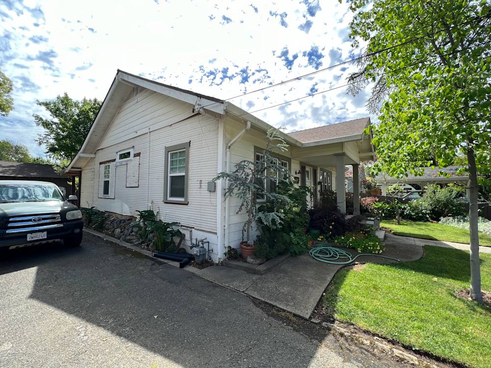 Worn white exterior with overgrown plants and cracked walkway in Sacramento neighborhood