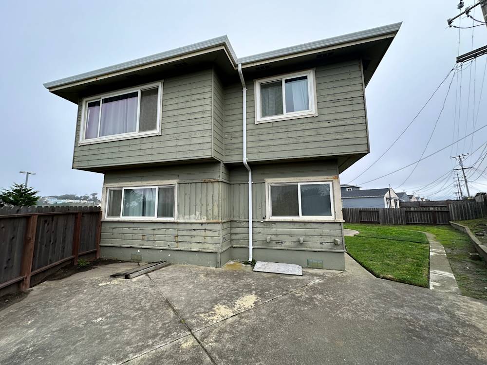 Worn, dated two-story home with gray siding and weathered exterior