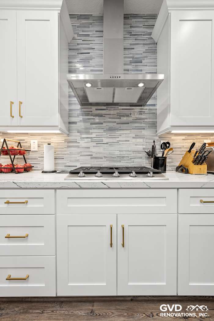 Modern kitchen featuring white custom cabinets, Cambria countertops, and a stylish gray backsplash with brass hardware