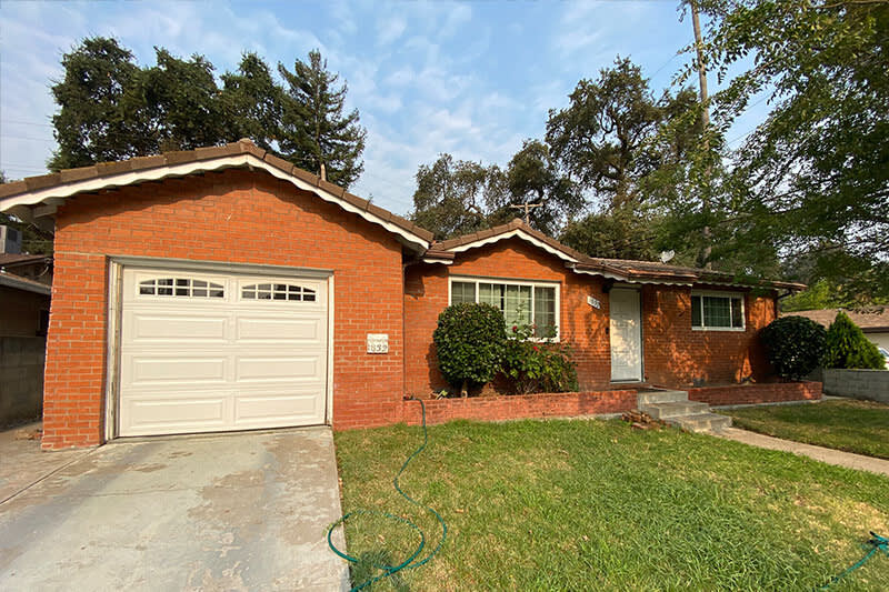 Brick exterior with outdated style, overgrown shrubs, and worn garage area