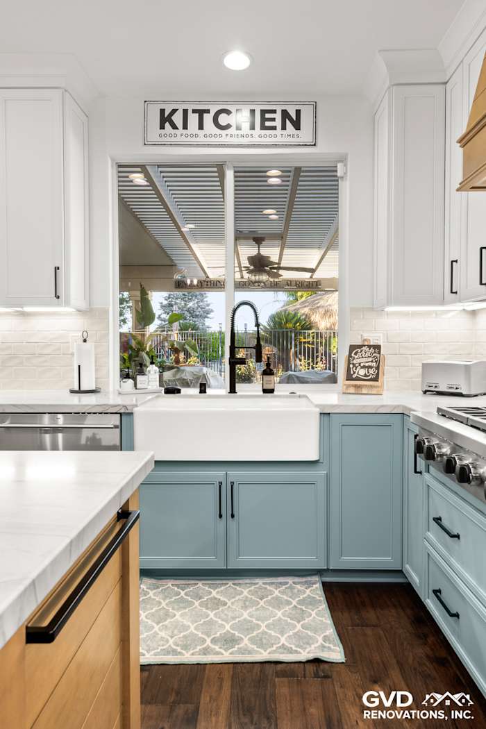 Modern kitchen featuring blue base cabinets, white quartz countertops, and farmhouse sink with window view