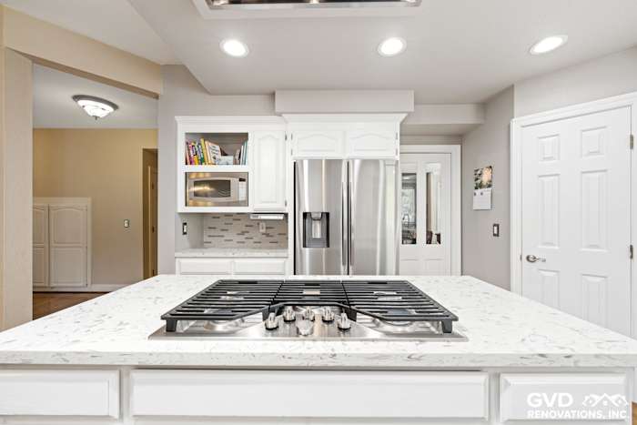 Modern kitchen with white cabinetry, quartz island, stainless steel appliances, and contemporary lighting fixtures
