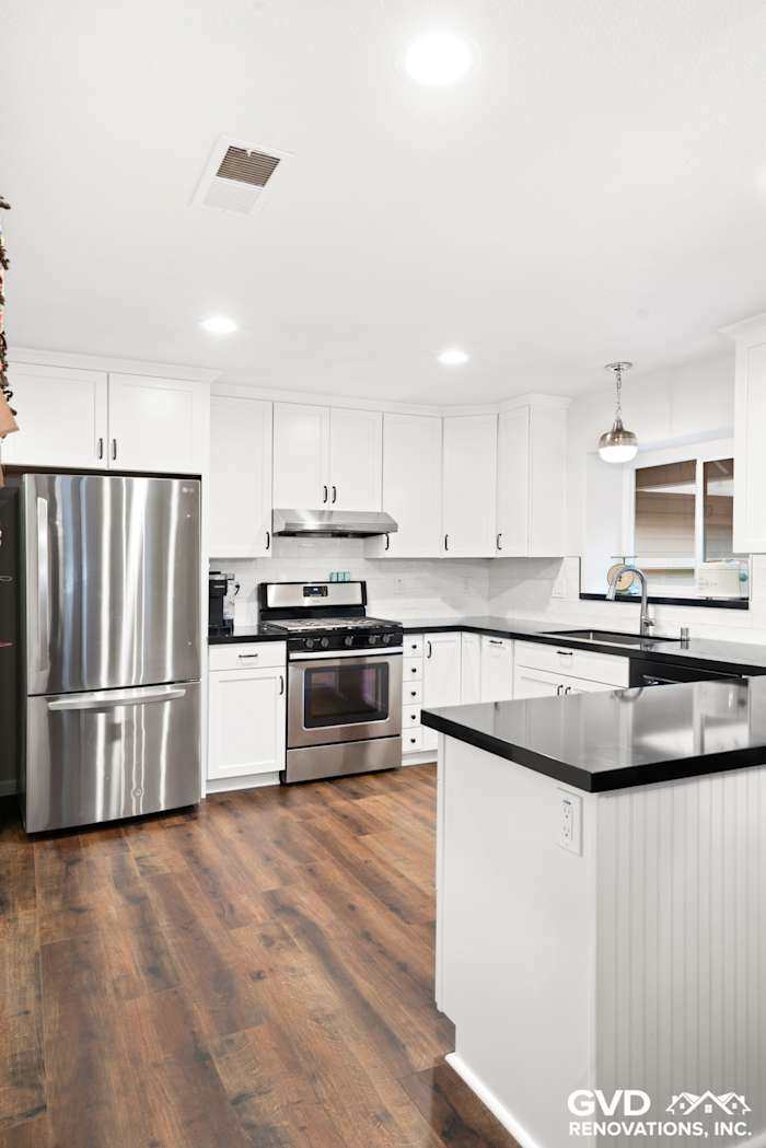 Bright white shaker kitchen featuring stainless steel appliances, black countertop, and wooden floors in Loomis, CA