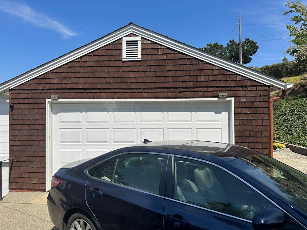 Single-story garage with brown shingle siding and white garage door in Sacramento