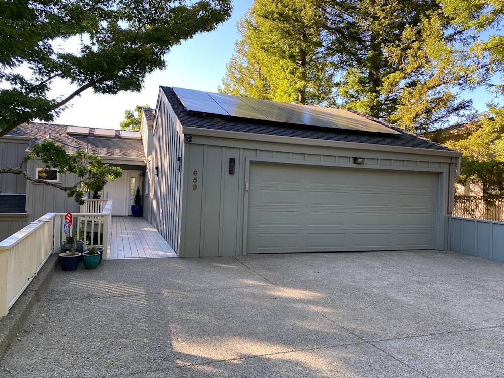 Concrete driveway leading to a modern garage in Sacramento with solar panels and landscaped greenery