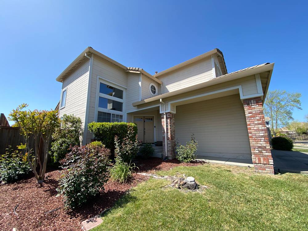 Two-story home with light siding and brick accents, surrounded by landscaped garden in Sacramento