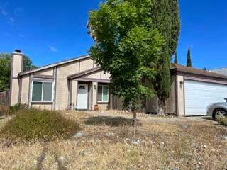 Unkempt front yard with dry grass, beige exterior, and overgrown shrubs in Sacramento
