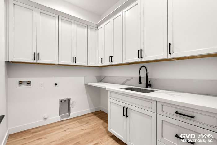 Bright laundry room with white cabinetry, quartz countertop, and black faucet in new construction home
