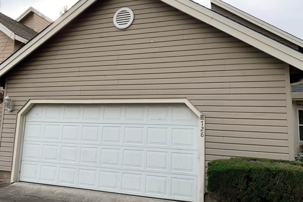 Worn, beige siding and plain white garage door on a suburban home