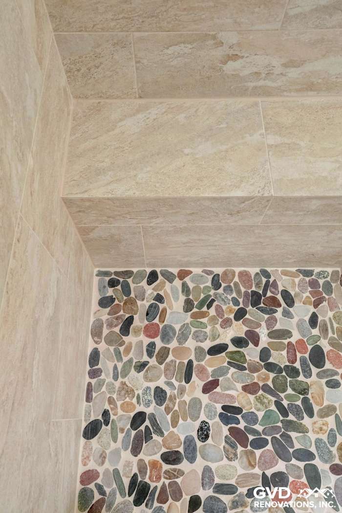 Textured stone tile shower wall with multicolored pebble flooring in renovated Fair Oaks bathroom