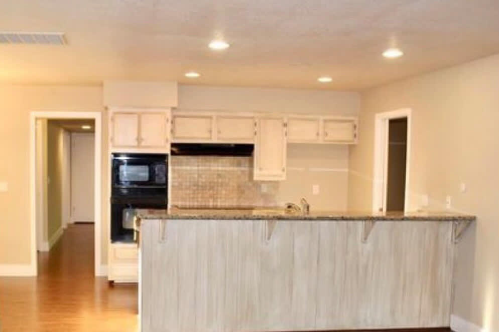 Outdated kitchen with worn cabinets, dark appliances, and beige walls