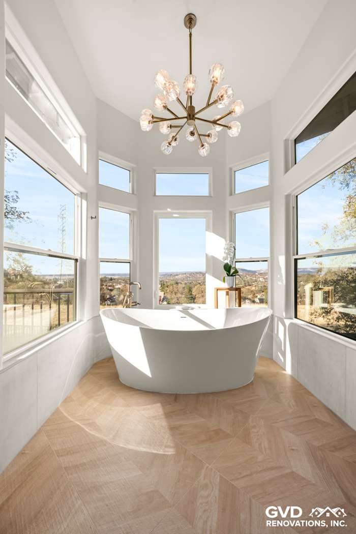 Bright master bathroom featuring a freestanding BainUltra air jet tub, large windows, and elegant chandelier