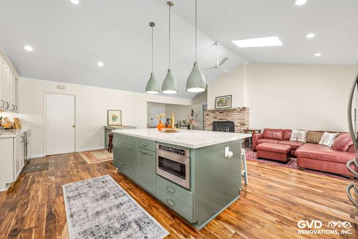 Modern kitchen remodel featuring a custom green island with quartz countertop, pendant lights, and hardwood floors
