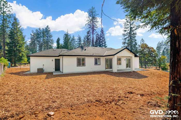 Modern single-story home exterior with white stucco, black roof, and surrounded by forested landscape in Paradise, CA
