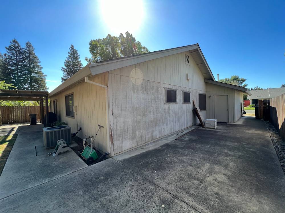 Weathered exterior of a Sacramento home with concrete driveway and bright sunlight
