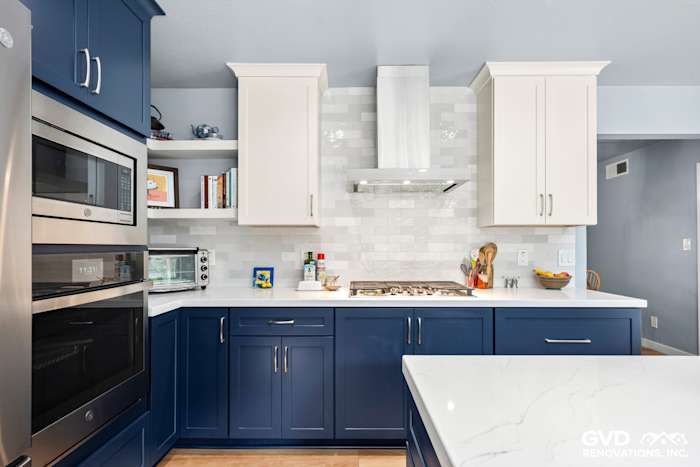 Modern kitchen with blue and white cabinetry, quartz countertop, stainless steel appliances, and glass tile backsplash