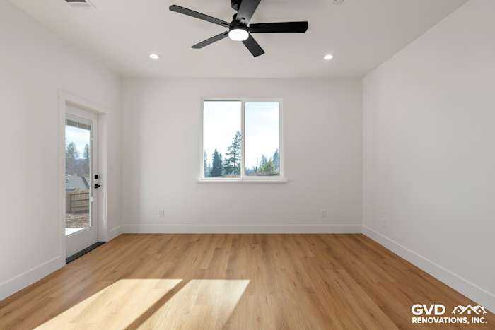 Bright, spacious interior room with light wood flooring, large window, and modern ceiling fan