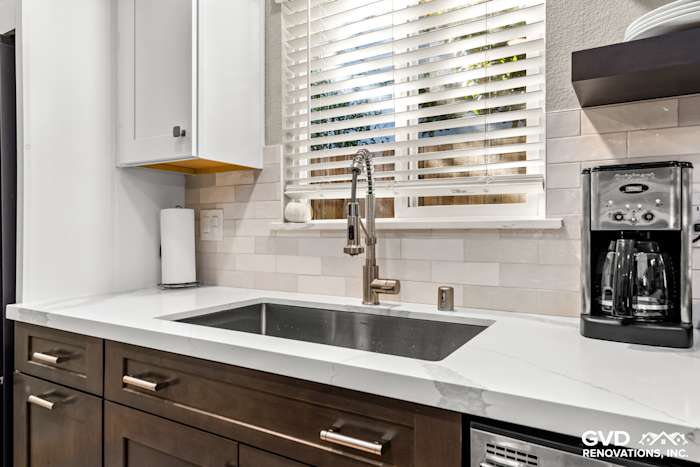 Modern kitchen sink area featuring a gray quartz countertop, white cabinetry, and stainless steel faucet