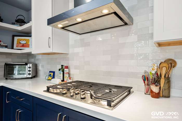 Modern kitchen with blue cabinets, stainless steel gas range, white subway tile backsplash, and quartz countertop