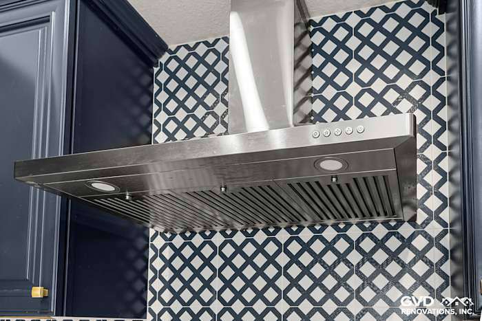 Modern kitchen range hood above navy blue cabinets with geometric backsplash tiles in Sacramento remodel