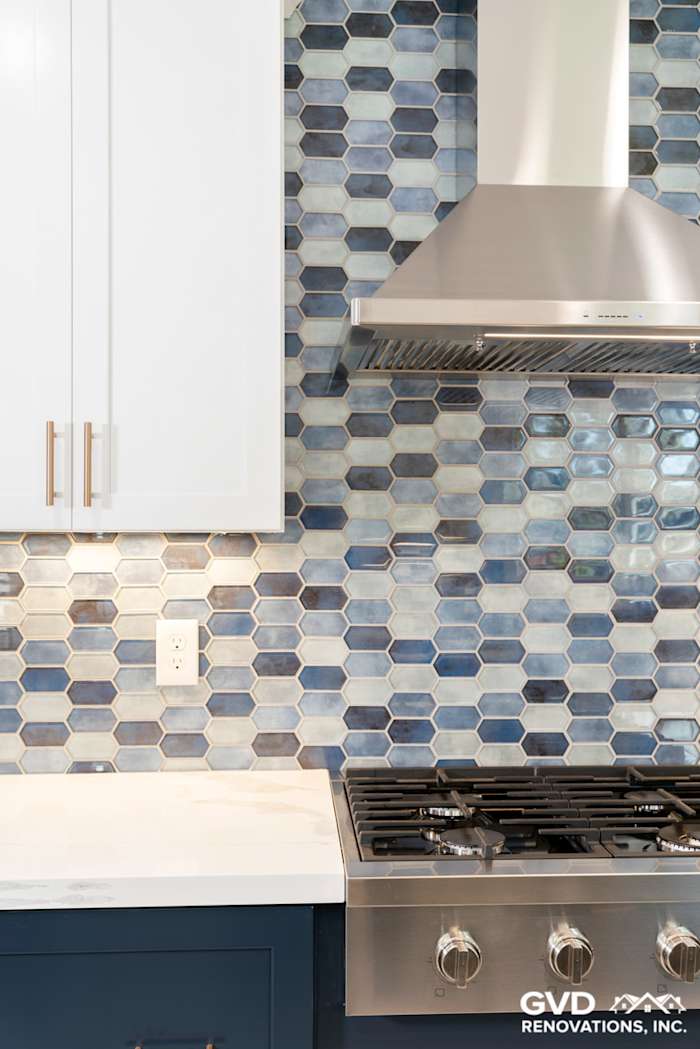 Modern kitchen with hexagonal blue and gray backsplash, stainless steel range hood, and white cabinetry