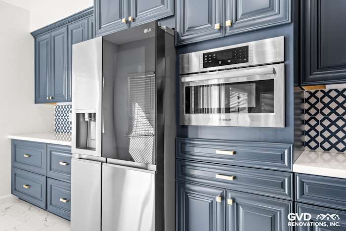 Stylish blue kitchen cabinetry with quartz countertops, stainless steel refrigerator and microwave, and patterned backsplash