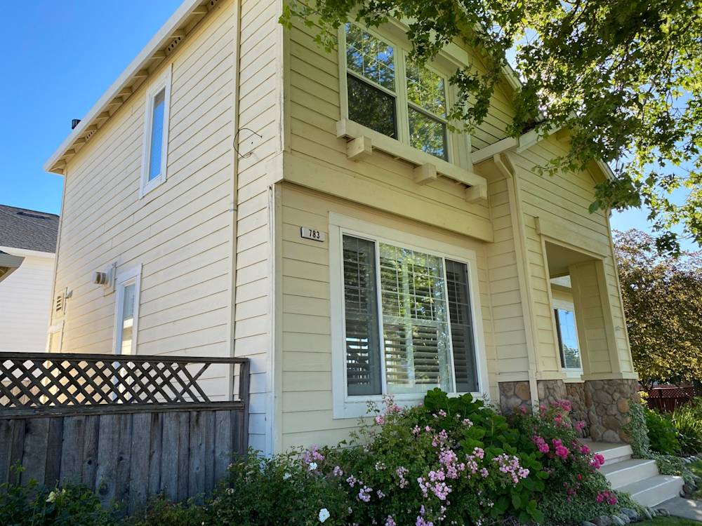 Light yellow exterior with white trim, stone accents, and vibrant flower beds in Sacramento