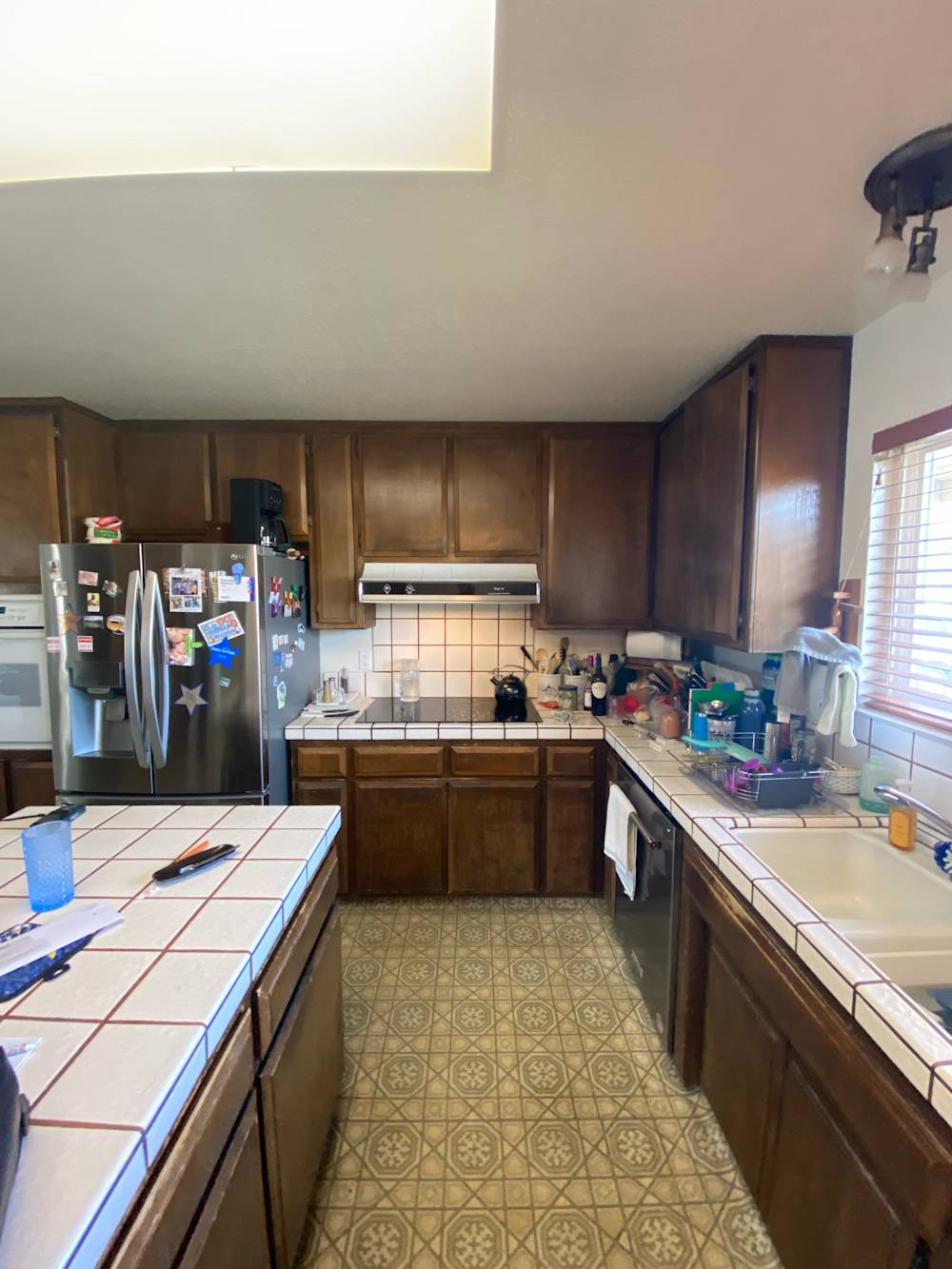 Dark wood cabinetry and dated tile countertops in cramped kitchen