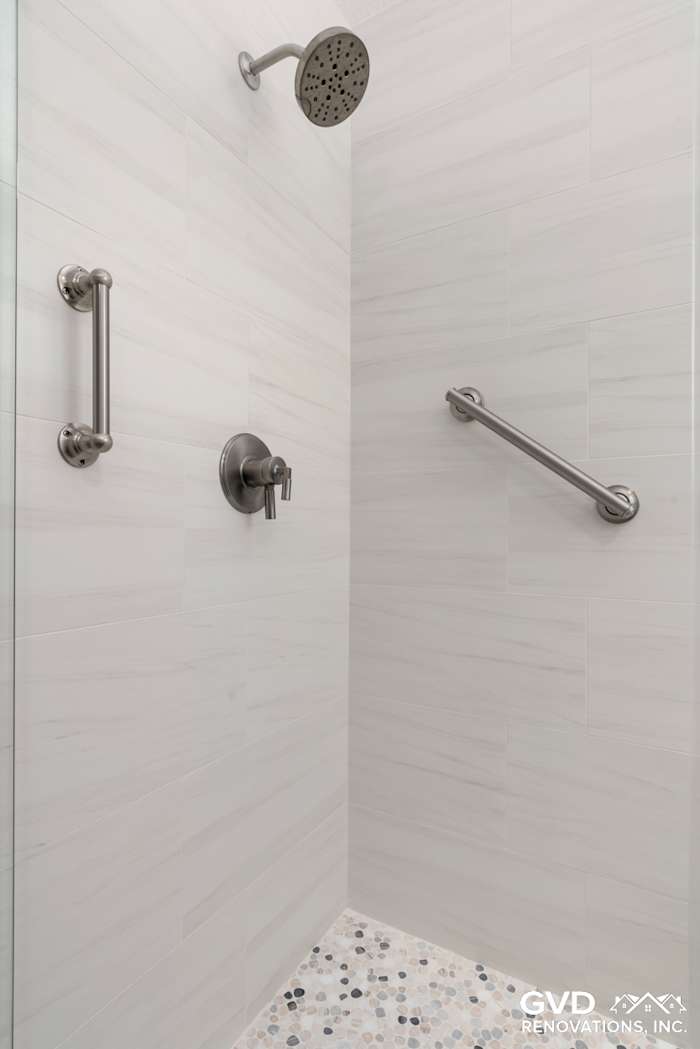 Modern shower renovation with sleek tile, grab bars, and pebble floor in a Rocklin bathroom