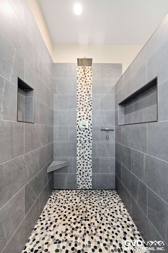 Modern master bathroom shower featuring grey tile walls, pebble floor, and niche storage in El Dorado Hills