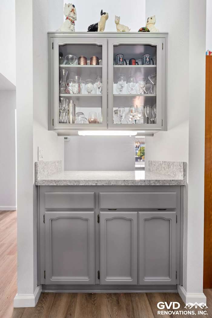 Remodeled kitchen in Carmichael with gray cabinetry, granite countertop, and glass-front cabinet showcasing dishware
