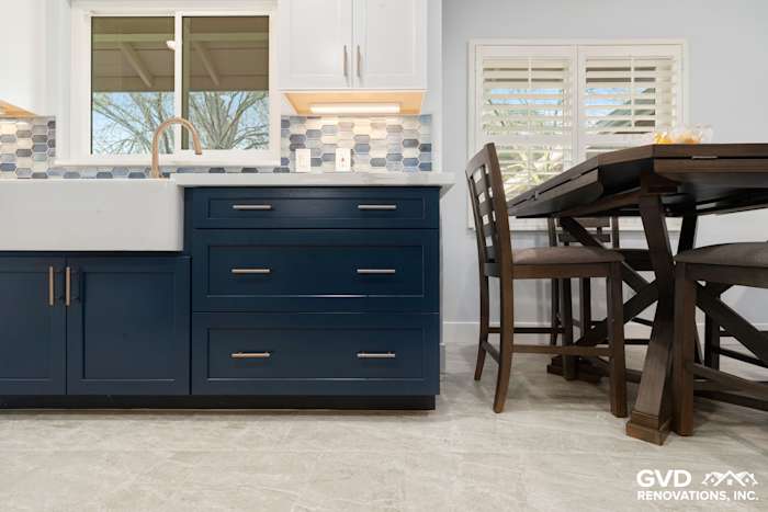 Dark blue kitchen cabinets with a farmhouse sink and light gray tile floor in a remodeled Sacramento kitchen