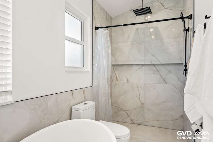 Modern bathroom featuring marble wall tiles, a freestanding tub, glass shower, and dual vanity in Antelope home