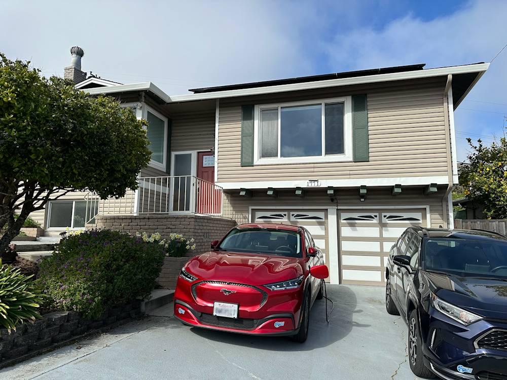 Front exterior of a Monterey home with beige siding, green shutters, and a red car in the driveway