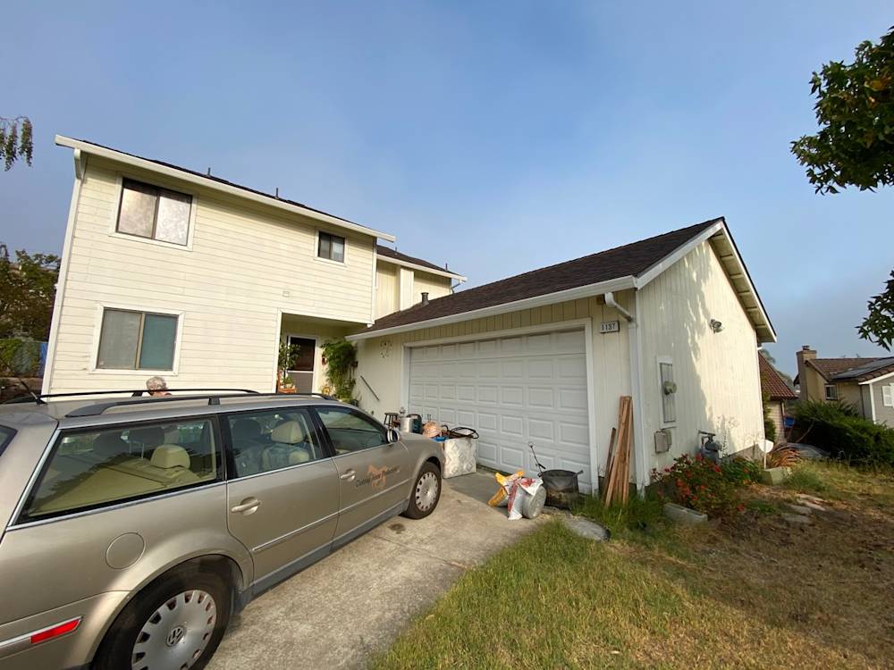 Exterior view of a two-story home in Sacramento with overgrown yard and cluttered driveway