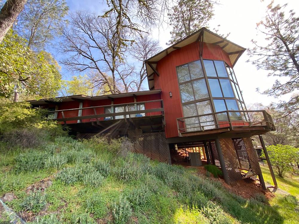 Red wood exterior and expansive windows on a sloped hillside in Northern California