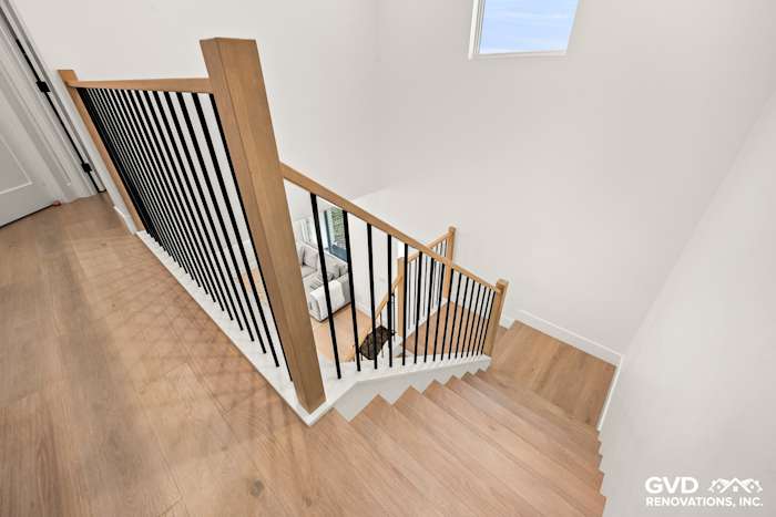 Renovated staircase with wooden railings and black balusters, leading to a bright living area in Antelope, CA
