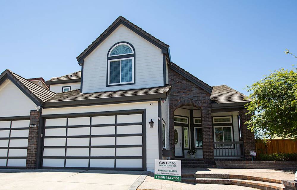 Updated home exterior featuring modern white siding, sleek garage door, and fresh landscaping