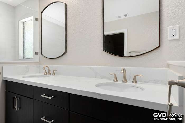 Modern bathroom featuring a double vanity with quartz countertop, dark cabinetry, and oval mirrors
