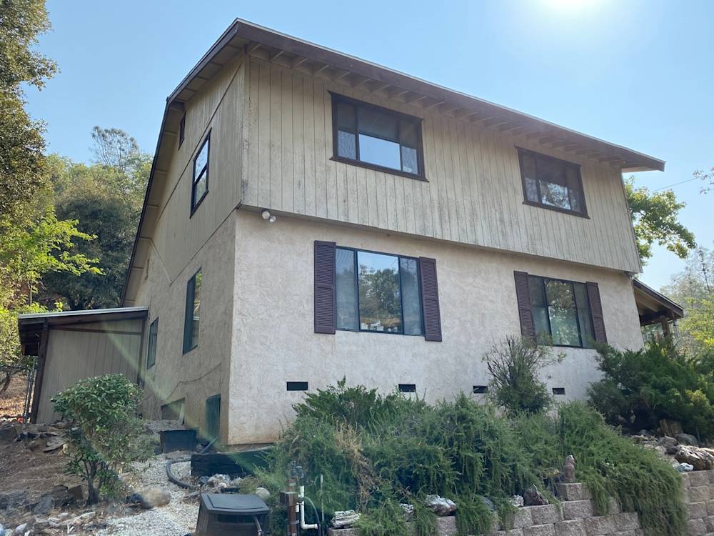 Stucco exterior with wooden accents, overgrown shrubs, and uneven landscaping in Northern California