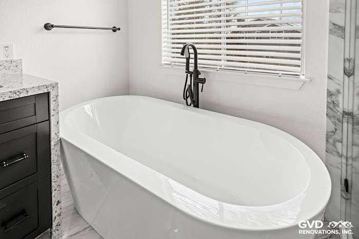 Modern bathroom featuring a freestanding white soaking tub, custom cabinetry, and sleek black faucet