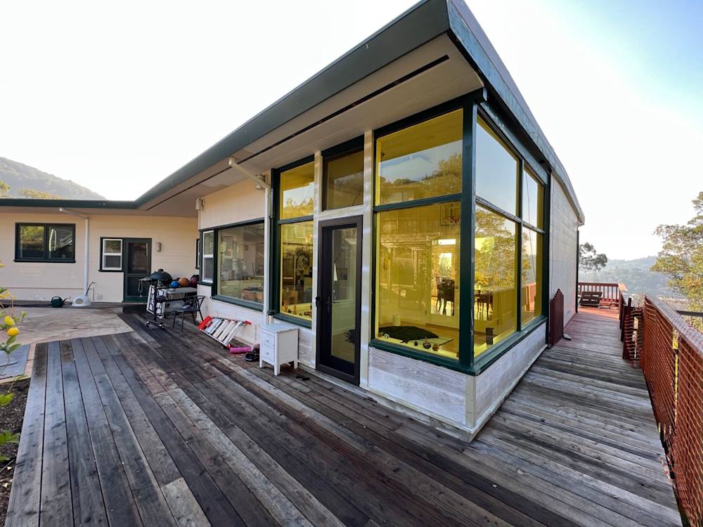 Modern home exterior with large windows, wood deck, and natural landscape in Northern California
